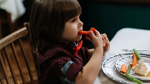 A young child eats fresh vegetables at the dining table.