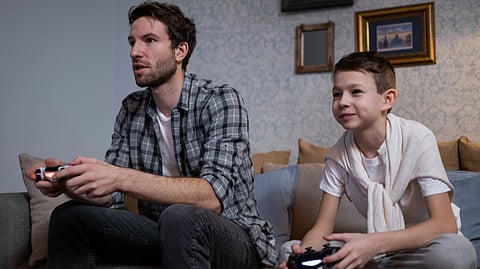 A man and boy play a video game together on a couch.
