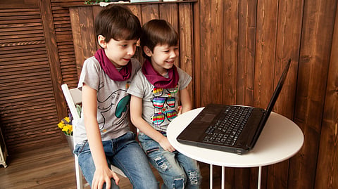 Two young boys smile while using a laptop together.