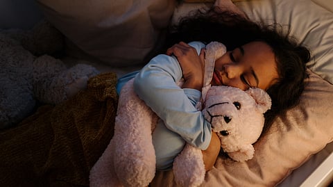A young child sleeps peacefully while hugging a pink teddy bear in a cozy bed.
