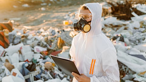 An inspector in protective gear checks a landfill filled with plastic waste.