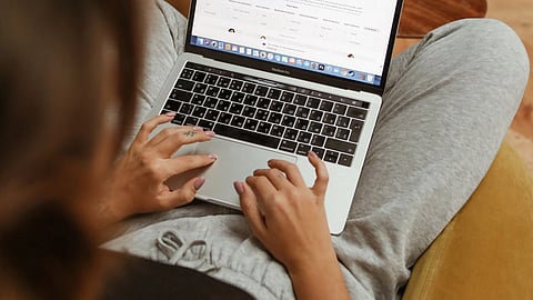 A person sits on a yellow chair while using a laptop.