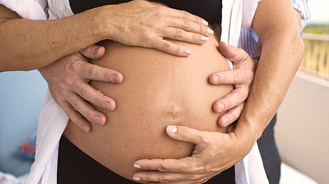Hands gently resting on a pregnant belly.