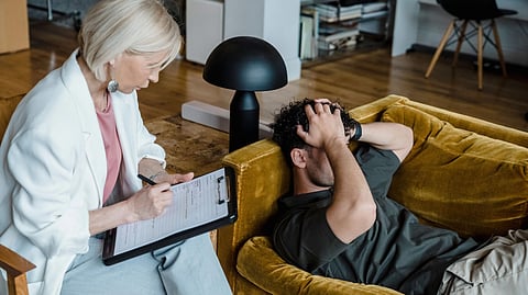 A therapist takes notes while a distressed man lies on a sofa during a counseling session.