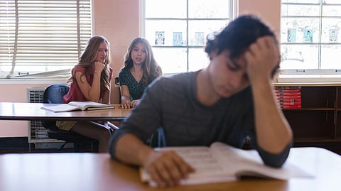 A student looks stressed while sitting at a classroom desk.