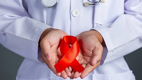 A healthcare worker holds a red HIV awareness ribbon.