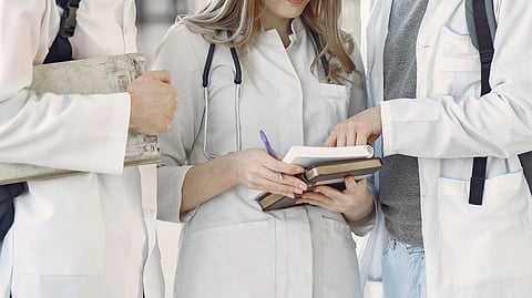 Three medical graduates standing together and reading a book.