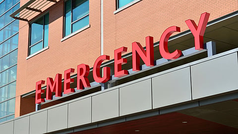 A low-angle view of a large red “EMERGENCY” hospital sign.