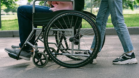 A person in a wheelchair moves alongside a companion on a paved path.