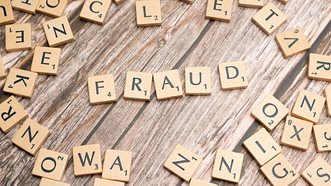 Scrabble tiles spell "FRAUD" on a wooden surface.