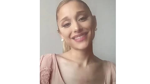 Ariana Grande smiles at the camera in a pink outfit with her signature high ponytail.