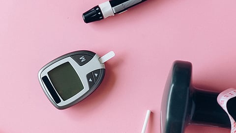 A blood glucose meter with a test strip on a pink background.