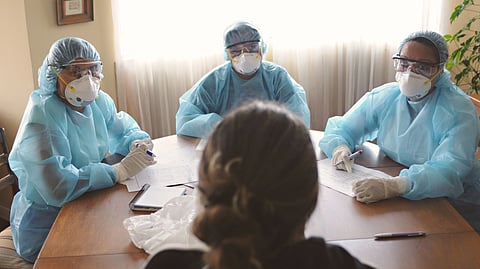 Three healthcare workers in PPE meet with a patient.
