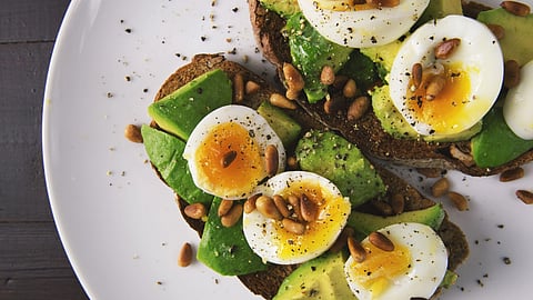 Avocado toast with soft-boiled eggs and pine nuts on a plate.