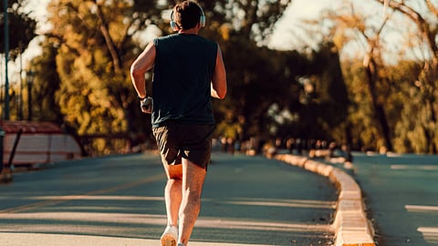 A man runs along a tree-lined road while wearing headphones.