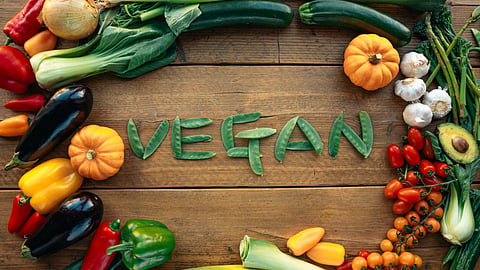 An overhead view of fresh vegetables with the word “VEGAN” spelled out in green peas.
