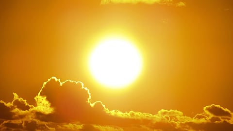 A bright sun shining through an orange sky with dark clouds.
