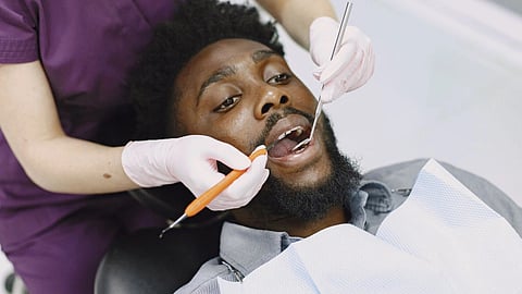 A bearded man receives a routine dental examination in a dental chair.