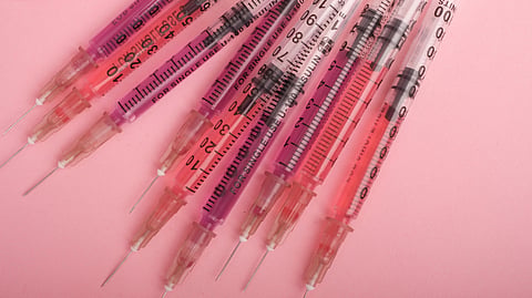 Several insulin syringes lie on a pink background.