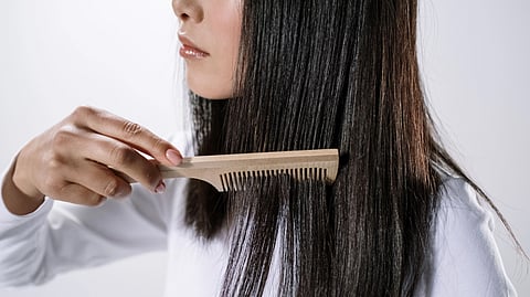 Woman gently combing her long hair with a wide-toothed wooden comb.