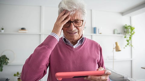 Older man looks concerned while viewing a tablet at home.