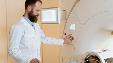 Medical technician adjusts an MRI scanner beside a patient.