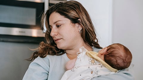 A mother lovingly cuddles her newborn in a home kitchen, showcasing tender motherhood moments.
