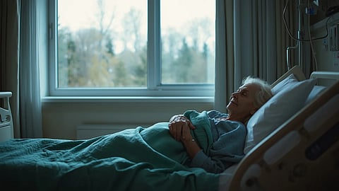 An elderly woman lying in a hospital bed of geriatric emergency care, appearing calm, with a blanket covering her and medical devices nearby.
