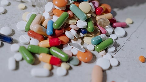Colorful pills and capsules spill from beneath white textured fabric on a gray surface.
