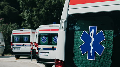An ambulance with a Star of Life symbol is parked in the foreground.