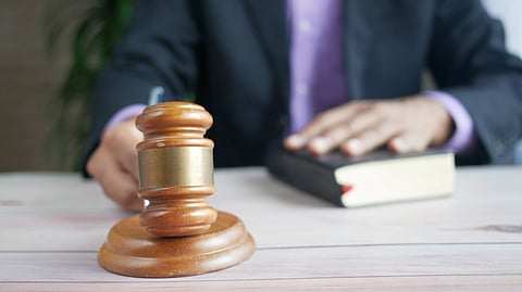 A brown gavel and a judge sitting behind.