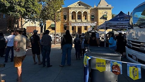 busy outdoor street market in bright daylight, set in front of a historic, ornate brick building.