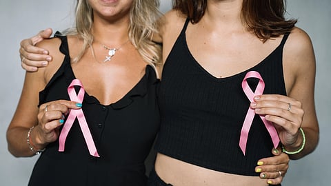 Two women smile together while holding pink breast cancer awareness ribbons.