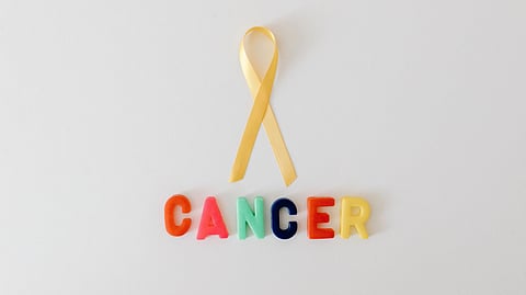 Yellow cancer awareness ribbon with colorful letters spelling 'cancer' on white background.