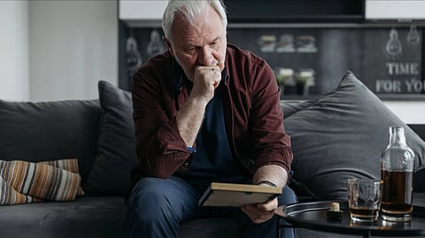 A senior adult man sitting on a couch, lost in thought while reading a book indoors.