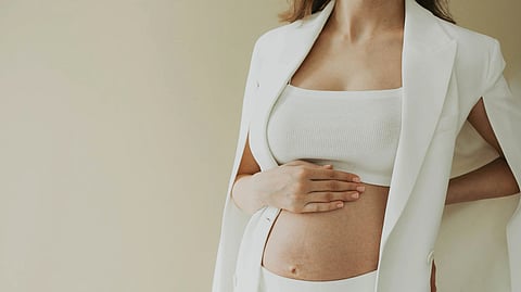 Close-up of a pregnant woman in fashionable attire posing in a studio setting
