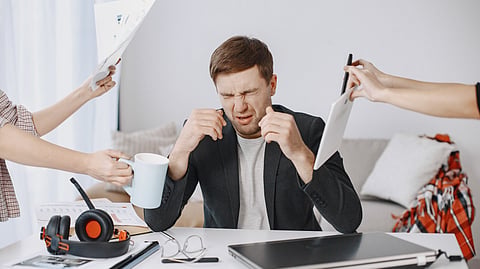 Adult man stressing out at home office desk with multiple demands surrounding him