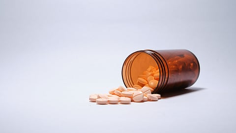 Closeup shot of pink tablets fallen out brown bottle on white surface