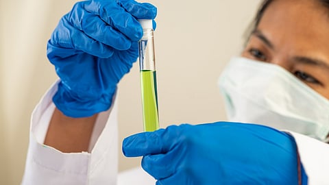 Scientists wear masks and gloves holding test tube with green liquid