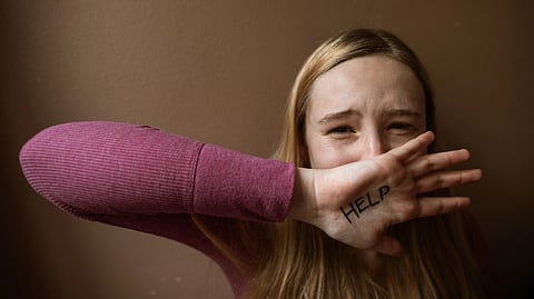 Girl with help written on her hand hiding her face with it