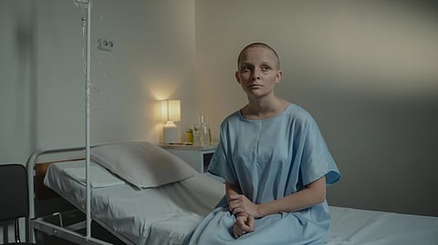 A thoughtful woman in a hospital gown sits on a bed, conveying calmness and reflection