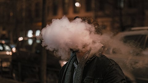 A man vaping and smoke in front of his face.