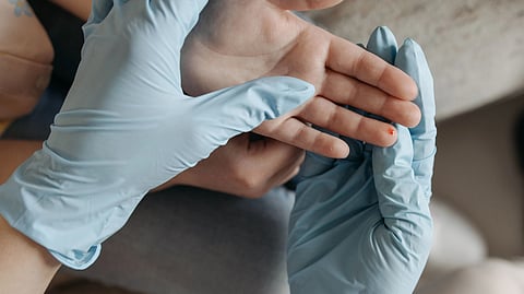 hands wearing blue gloves holding hand with blood on finger