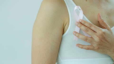 Woman holding breast cancer ribbon - baby pink - next to her chest