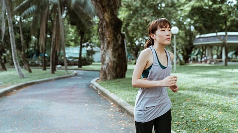A young woman jogging on a quiet park path surrounded by lush greenery