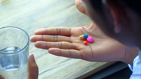 A hand holding a variety of pills alongside a glass of water, emphasizing health and medication