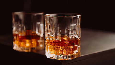 Crystal glasses filled with whiskey on a dark wooden surface, highlighting texture and color