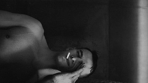 Black and white portrait of a man smoking in the shower with eyes closed, creating a moody atmosphere