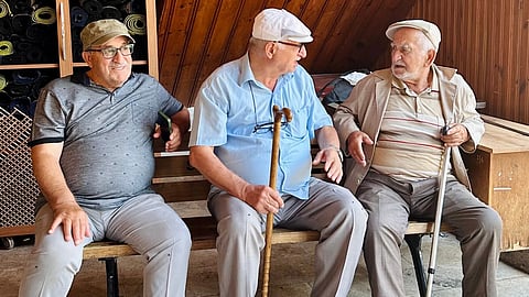 Three elderly men sitting and chatting on a bench indoors