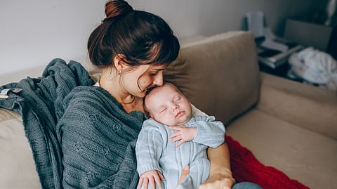A mother lovingly holds her sleeping baby on a cozy sofa, wrapped in warmth and affection